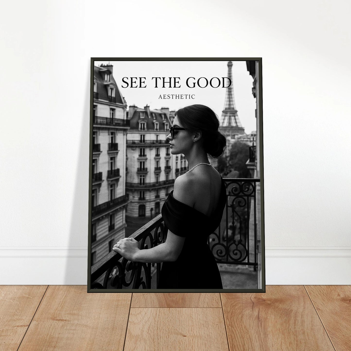 Paris Noir black and white Paris wall art in black metal frame, “See The Good” poster styled on wooden floor against wall